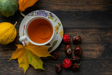 A cup of hot aromatic tea with lemon set on dry autumn leaves and chestnuts on a wooden table