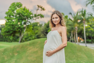 Pregnant woman hugging her tummy standing outdoors surrounded by nature. Pregnancy, expectation, motherhood concept