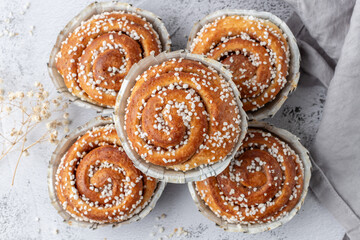 Fresh baked cinnamon buns rolls with grey linen napkin on grunge stone table background. Traditional swedish sweet pastry kanelbulle.