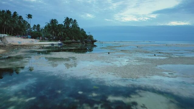 Filipino kids playing at sunset on Tubod beach, Siquijor island, Philippines. Slow aerial travelling. Low altitude drone view. Dogs running. Vibrant cloudy sky colors. Famous travel destination.