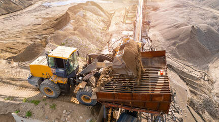 Mining excavator loading sand on belt conveyor in opencast, aerial top view. Open pit mine concept