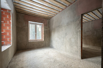 Renovation of a room in a modern house under construction. The walls are made of cement masonry, plastic Windows. Cement floor screed.