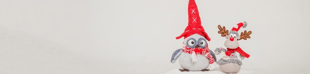 A toy figure of an owl and deer in a red hat. Isolated on a grey background. christmas decorations:, bird with santa hat.gift for the holiday. copy space. web banner