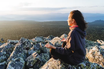Fotobehang Portrait of a girl in the mountains practicing yoga and meditation. Side view of man sitting in lotus position, mountain landscape, sunrise on top of mountain. © Aleksey