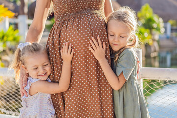 Sisters' love blooms as they tenderly embrace their mother's pregnant belly, sharing anticipation and affection for their soon-to-arrive sibling - obrazy, fototapety, plakaty