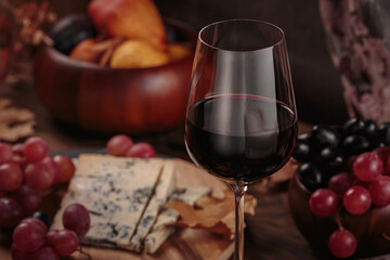 Glass of red wine served with blue cheese on dark wooden background. Autumn picnic with wine and cheese platter, fruits and dry leaves in rustic style