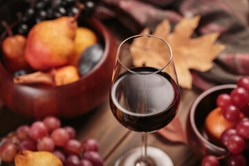 Glass of rich red wine served with fruits on dark wooden background. Autumn still life with wine, grapes and dry leaves in rustic style. Sweater weather concept