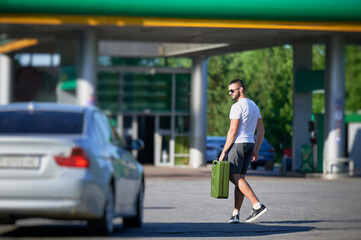 Confident man with canister finally found petrol station. Young male with empty canister in hand on background of gas station.