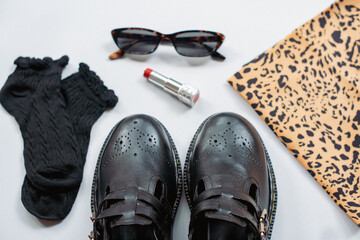 Flat lay photo concept of classic and fashionable women's fashion. Flatlay photo of vintage black mary jane shoes with socks, lipstick, glasses and leopard print bandana on clean white background