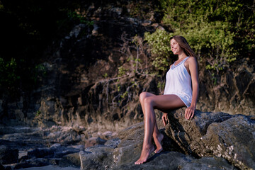 Outdoor portrait of beautiful young woman with long hair sitting on the rock.