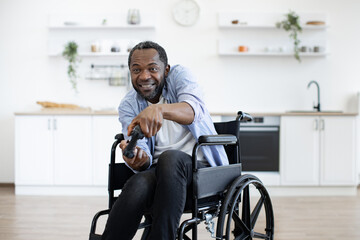 Close up view of african male gamer with mobility impairment with input devices in spacious kitchen...