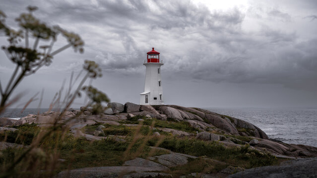 Photograph of a red and white lighthouse on a rock in the middle of nowhere. Grey and stormy weather 