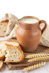 Clay retro jug of milk, sliced and bitten fresh baked spelt wheat loaf of bread on wooden cutting board