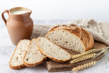 Sliced fresh baked spelt wheat loaf of bread on wooden cutting board with clay rural jug of milk,...