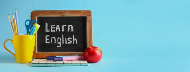 Stationery, apple and chalkboard with text LEARN ENGLISH on light blue background with space for...