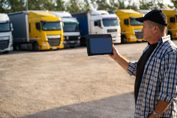 Man holding digital tablet, empty screen to add copy, trucks parked behind. Trucking app concept 

