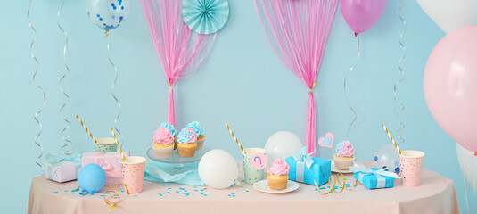 Tasty cupcakes with gifts for gender reveal party on table in room
