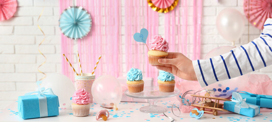 Woman taking tasty cupcake from table. Baby reveal party