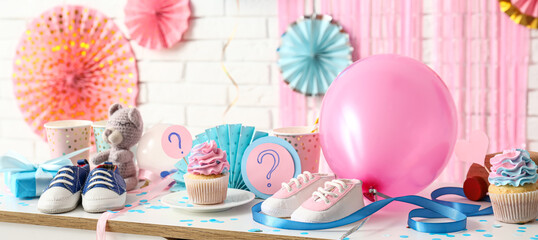 Tasty cupcakes with baby booties and gifts for gender reveal party on table