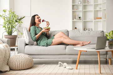 Young woman eating vegetable salad on sofa at home