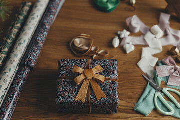 Merry Christmas! Wrapping christmas present. Stylish christmas gift, festive wrapping paper, ribbons, scissors, vintage ornaments and brass bells on wooden table. Winter holiday preparation