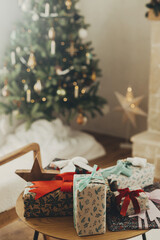 Naklejka na ściany i meble Stylish christmas gifts in festive wrapping paper with bows and vintage ornaments on wooden table on background of golden christmas tree lights.Happy holidays! Atmospheric christmas eve