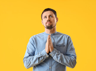 Handsome man praying on yellow background