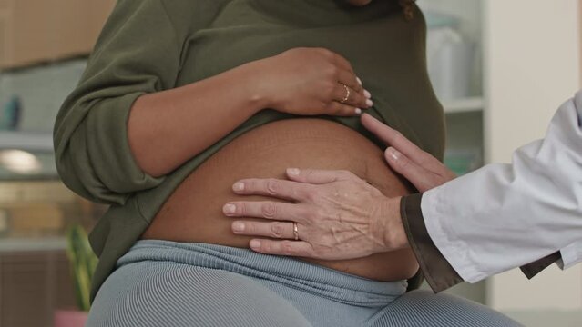 Cropped shot of unrecognizable female gynecologist palpating belly of pregnant woman doing checkup appointment in hospital