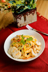 Tropical Pasta Salad With Mix Meat olive with shrimp and prawn served in bowl with flowers and fork isolated on red napkin side view of healthy green food on table