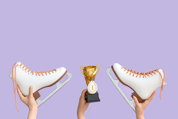Female hands with gold cup, medal and ice skates on lilac background