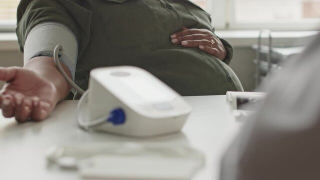 Over the shoulder cropped shot of unrecognizable obstetrician using tonometer while measuring blood pressure of pregnant woman during checkup appointment in clinic at daytime