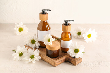 Wooden board with cosmetic products and chamomile flowers on light background