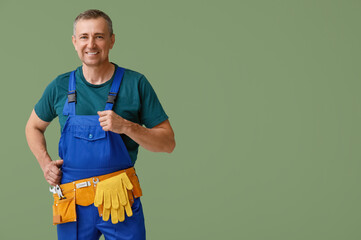 Portrait of male mechanic with tool belt on green background - obrazy, fototapety, plakaty