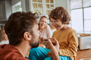 Happy young boy being messy during breakfast with his father in the kitchen