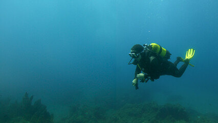 Scuba diver woman in motion, with a flashlight in her hand surrounded by a clean blue seabed near the bottom. Space for text, ads