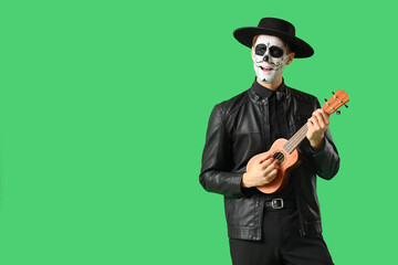 Young man with painted skull playing guitar on green background. Mexico's Day of the Dead (El Dia de Muertos) celebration