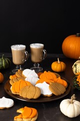 A plate of pumpkin-shaped cookies and a cup of latte on a dark background