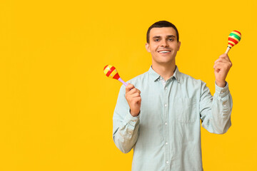 Handsome young man with maracas on yellow background