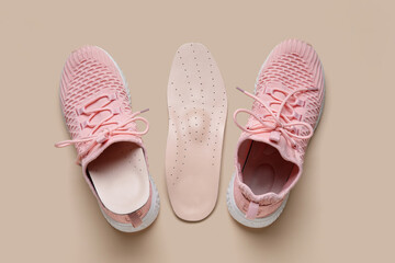 Pair of stylish pink sneakers with orthopedic insoles on beige background