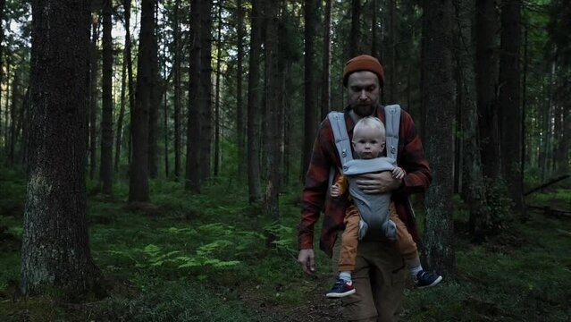 A male father with a child in a sling backpack walks through the forest