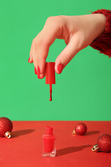 Female hand with red nail polish and Christmas balls on green background