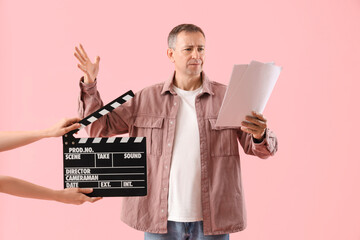 Mature actor reading film script and hands with clapperboard on pink background - Powered by Adobe