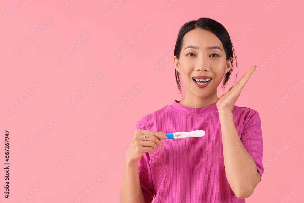 Poster Young Asian woman with pregnancy test on pink background