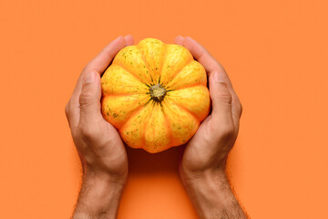 Male hands with fresh pumpkin on orange background