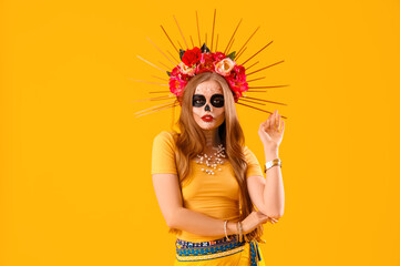 Beautiful young woman with painted skull on her face against yellow background. Celebration of Mexico's Day of the Dead (El Dia de Muertos)