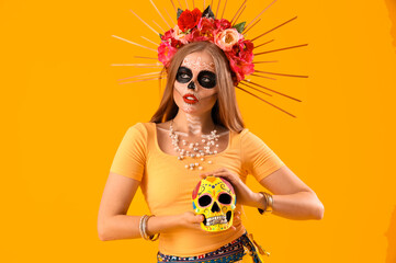 Beautiful young woman with painted skull on yellow background. Celebration of Mexico's Day of the Dead (El Dia de Muertos)