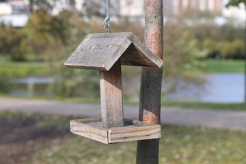 Wooden bird feeder with berries and wheat inside, birdhouse on a beautiful blurred background of yellow leaves outdoors. feeders in the autumn park.