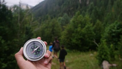 hand with compass and out of focus a family that is taking an excursion through a national park. Concept of family time in nature and national park. Finding the way, teamwork and solution orientation.