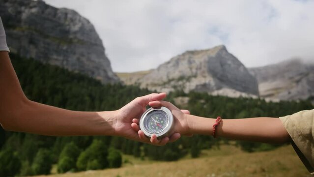 Close-up of a hand holding a compass against a nature background. A mother with children explores a mountain in search of direction. Mother's larger hands contrast with children's hands with compass