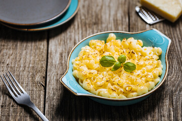 Mac and Cheese in blue bowl placed on rustic wooden board, with basil on top. 